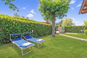 Ein Garten mit zwei Liegestühlen, einem Baum und einer Hecke.