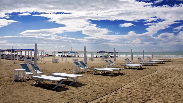 Une plage avec des transats et des parasols, un ciel dégagé et l’océan en toile de fond.