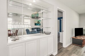 A modern kitchen with a glass partition, white cabinetry, and a dining area with blue chairs. - TB 24 three bedroom True Blue Condo (Pawleys Island)