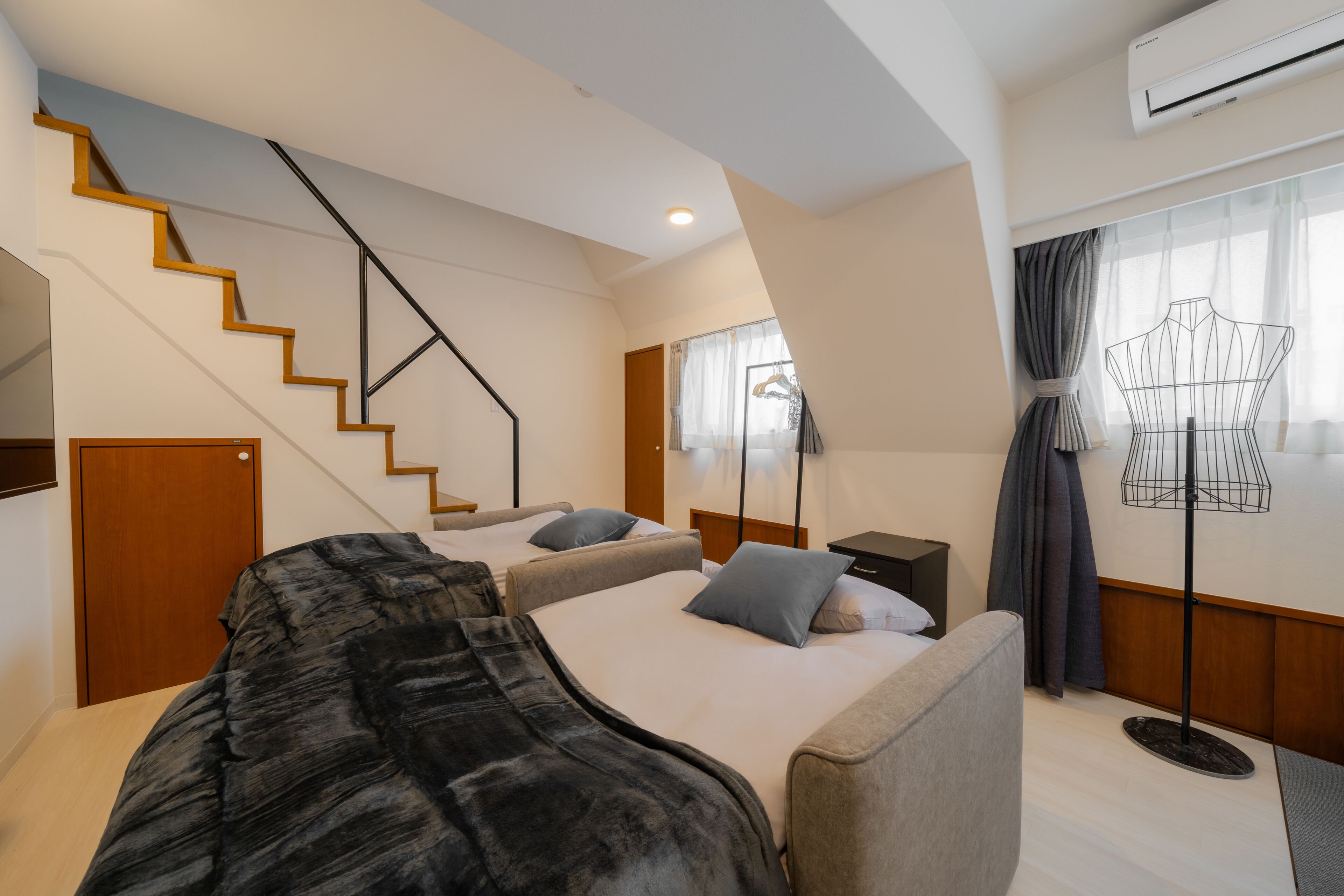 A hotel room with a staircase, two beds, a wardrobe, a desk, a lamp, and an air conditioning unit.