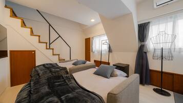 A hotel room with a staircase, two beds, a wardrobe, a desk, a lamp, and an air conditioning unit.