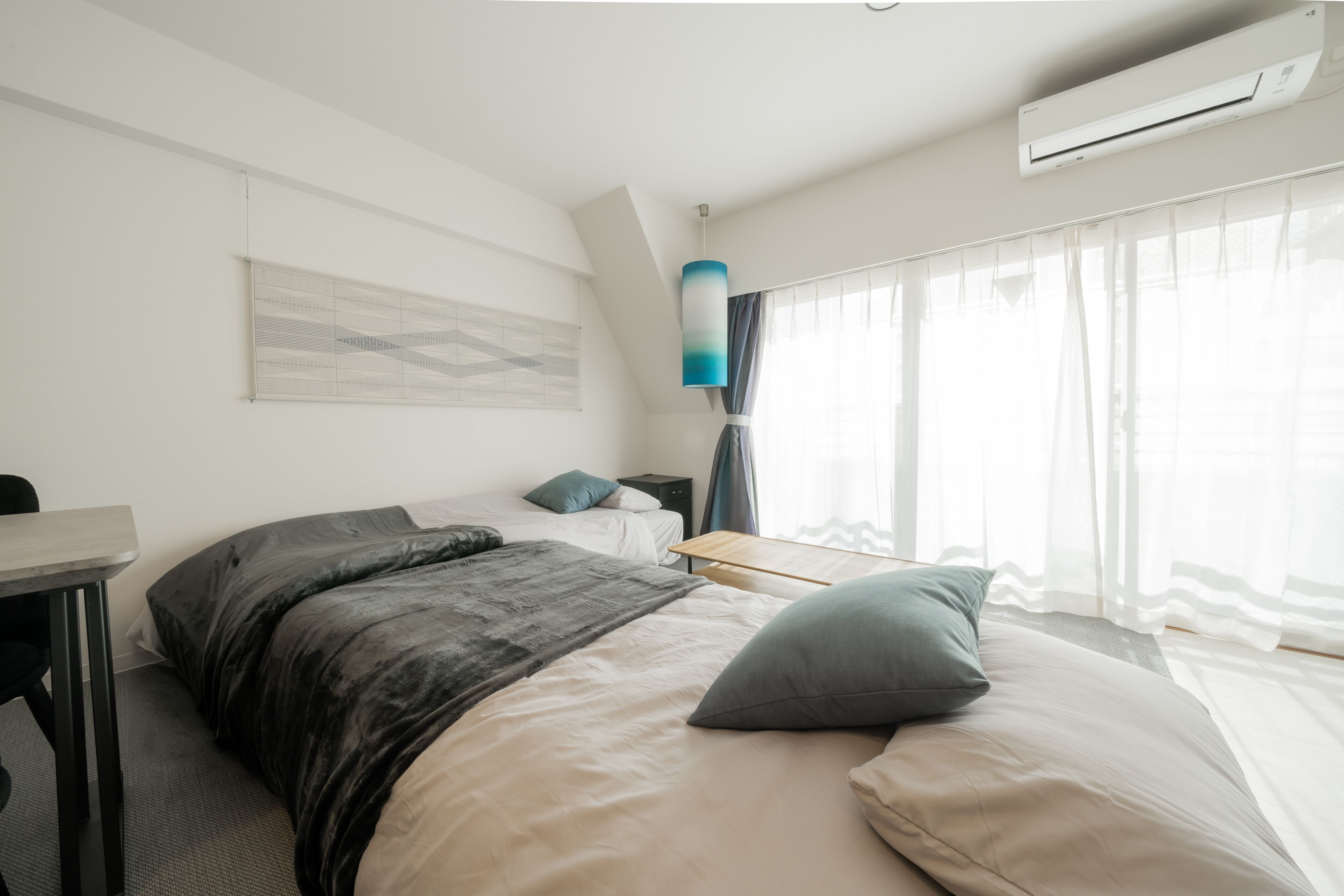A modern hotel room with a bed, a desk, a chair, a nightstand, and a window with curtains.
