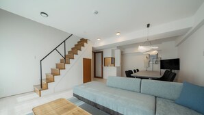 A modern living room with a staircase, a sofa, a dining table with chairs, and a flat-screen TV. - HOTEL LEGALIE Osaka Shinsaibashi North (Osaka)