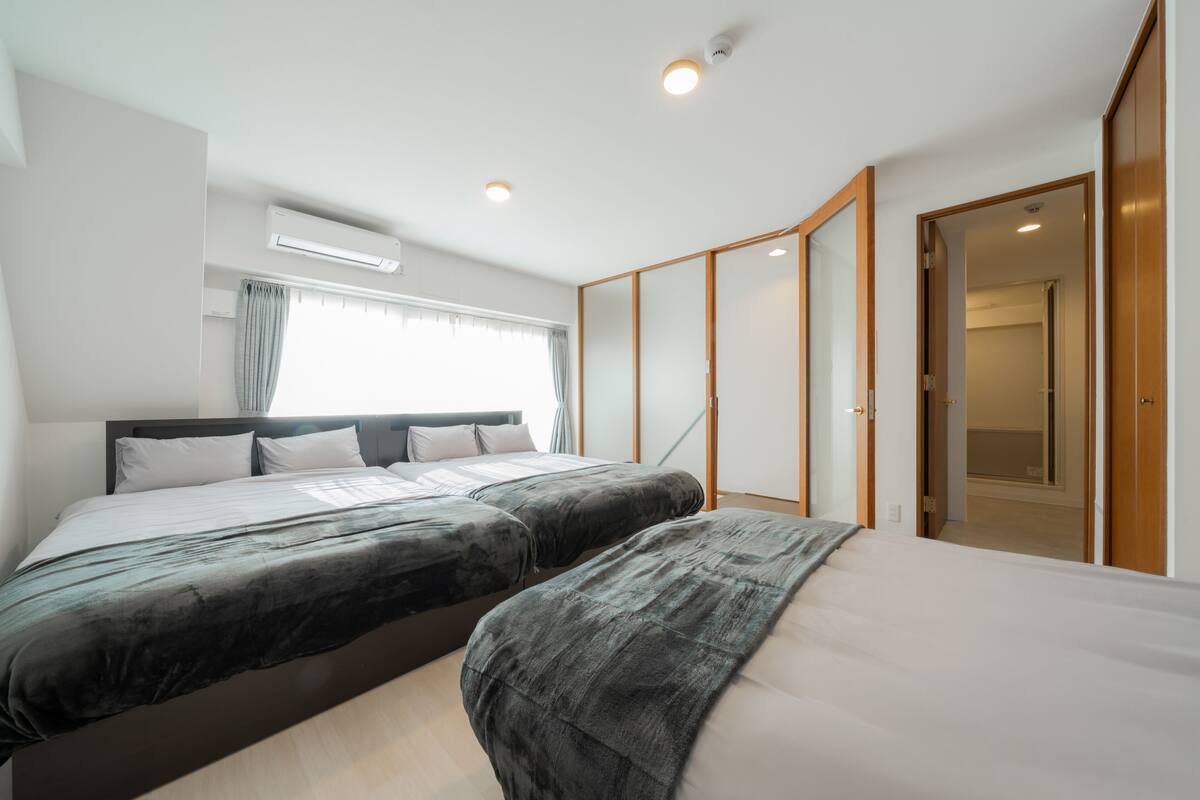 Una habitación de hotel moderna con dos camas, un ventanal con cortinas, un aire acondicionado y un armario de madera.