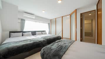 A modern hotel room with two beds, a large window with curtains, an air conditioning unit, and a wooden wardrobe.