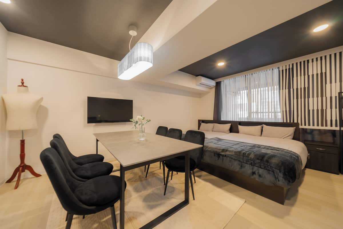 Un dormitorio moderno con una cama, mesitas de noche, un televisor, un escritorio con sillas y una lámpara.