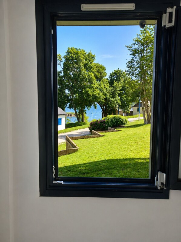 A window with a view of a grassy area, trees, and a body of water. - Sea-view house in an exceptional private estate (Douarnenez)