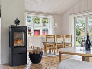 Ein gemütlicher Raum mit Kaminofen, einem Esstisch mit Stühlen, einem Fenster mit Vorhängen und einer Pendelleuchte.