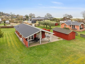 Ein Wohngebiet mit einem Haus, das eine überdachte Terrasse, einen roten Schuppen und eine Rasenfläche besitzt.