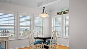 Uma área de refeições com uma mesa redonda, cadeiras brancas e vista para o oceano através de grandes janelas.