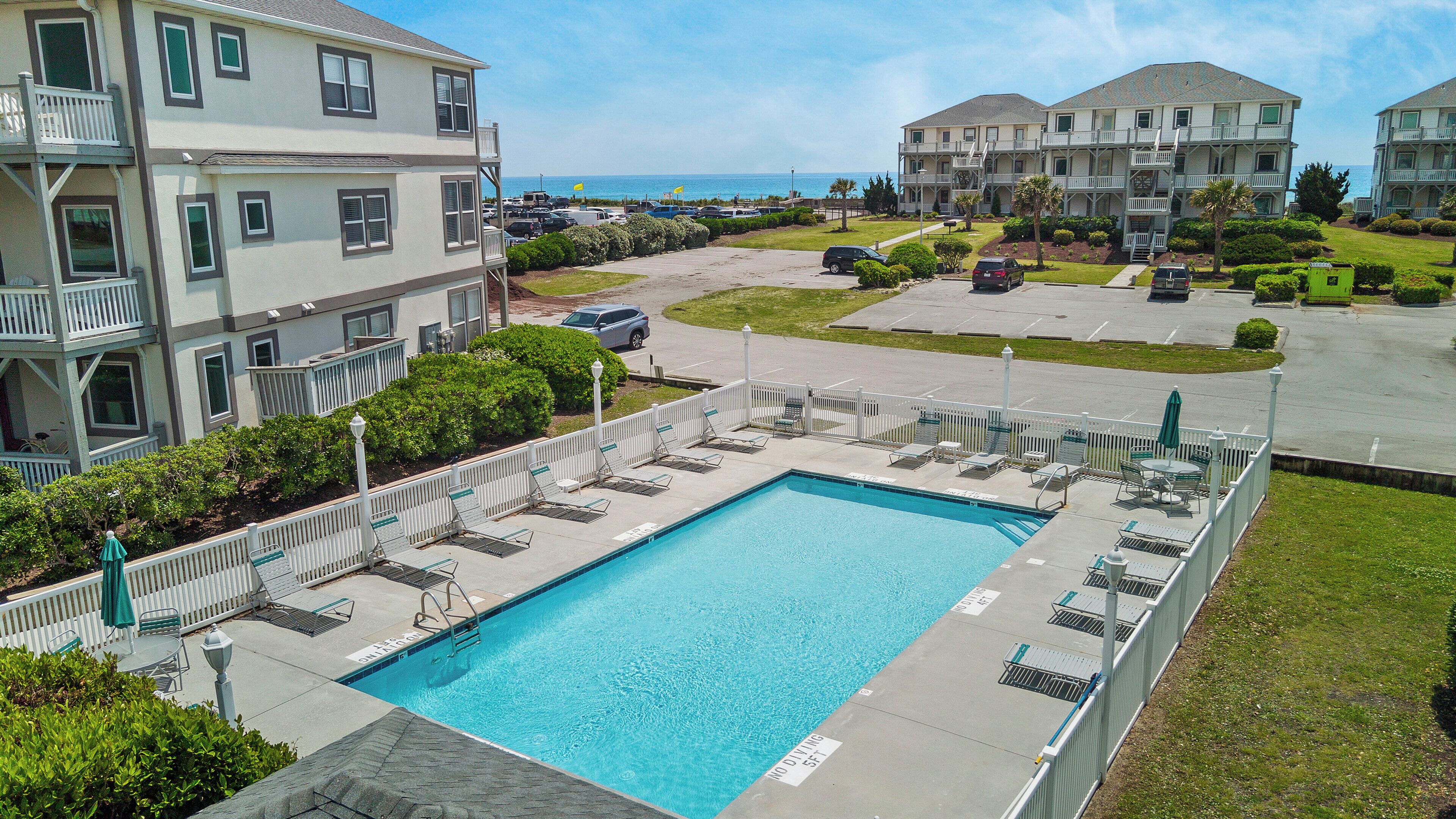 A swimming pool with lounge chairs and a no diving sign, surrounded by a fence and buildings with balconies.