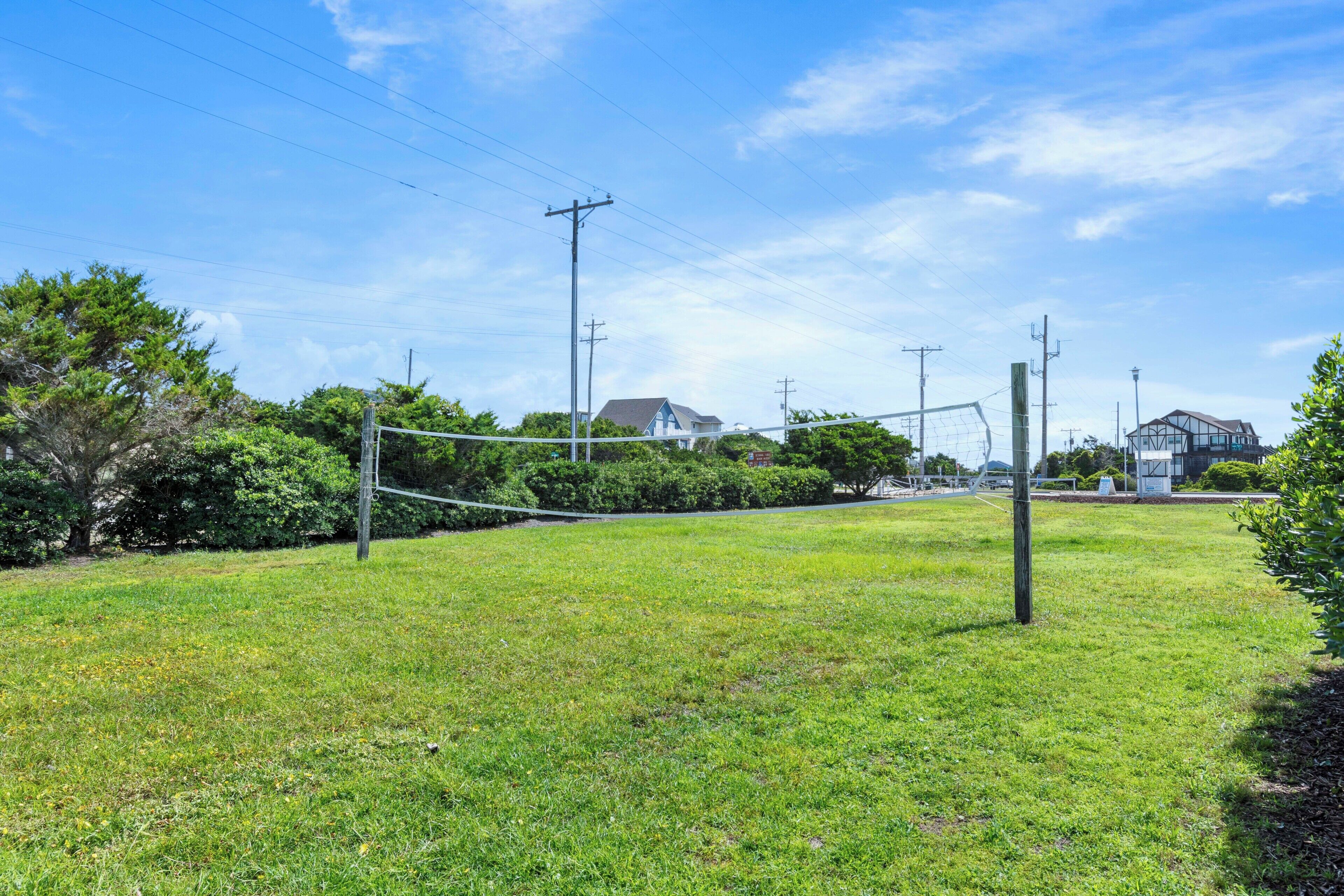 Une zone herbeuse avec un filet de volley-ball, entourée d’arbres et de poteaux électriques.