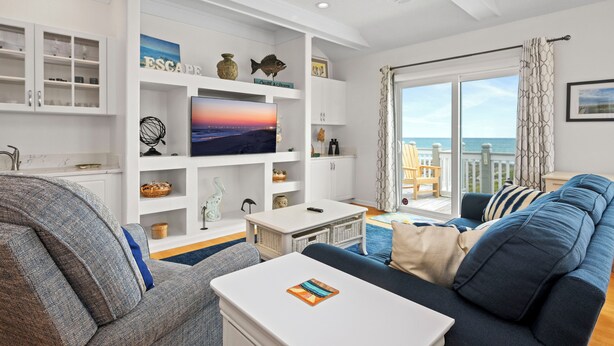 Sala de estar com televisão, armários brancos, sofá e vista para o mar.