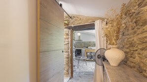 A rustic kitchen with stone walls, a wooden door, and a fan. - Charming Stone Cottage for Rent in a Picturesque Pyrenean Village (Glorianes)