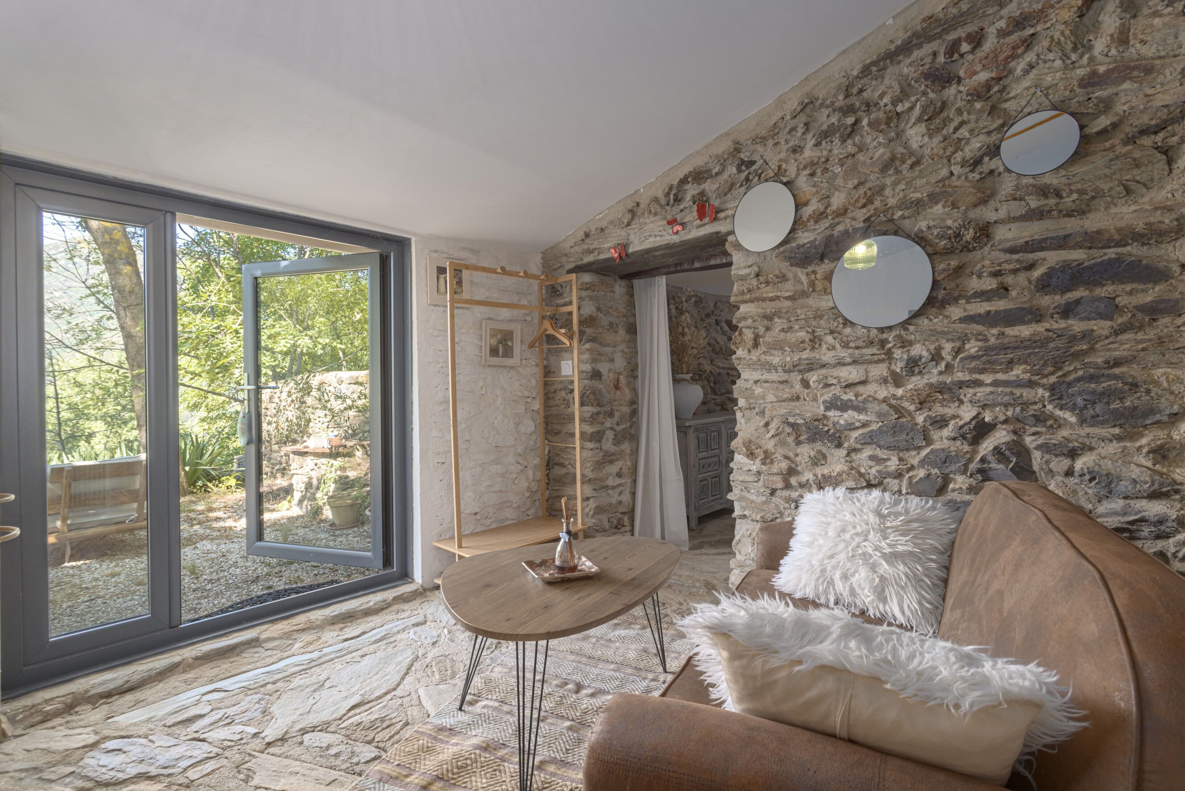 Une pièce avec un mur en pierre, une table en bois, un canapé et un luminaire suspendu.