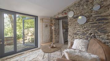 Une pièce avec un mur en pierre, une table en bois, un canapé et un luminaire suspendu.