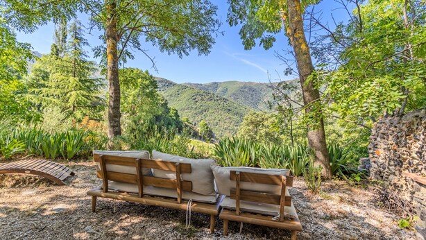 A wooden bench with cushions in a natural setting with trees and a view of hills. - Charming Stone Cottage for Rent in a Picturesque Pyrenean Village (Glorianes)