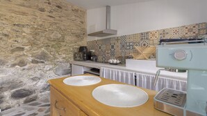 A kitchen with a stone wall, a coffee machine, and a tiled backsplash. - Charming Stone Cottage for Rent in a Picturesque Pyrenean Village (Glorianes)