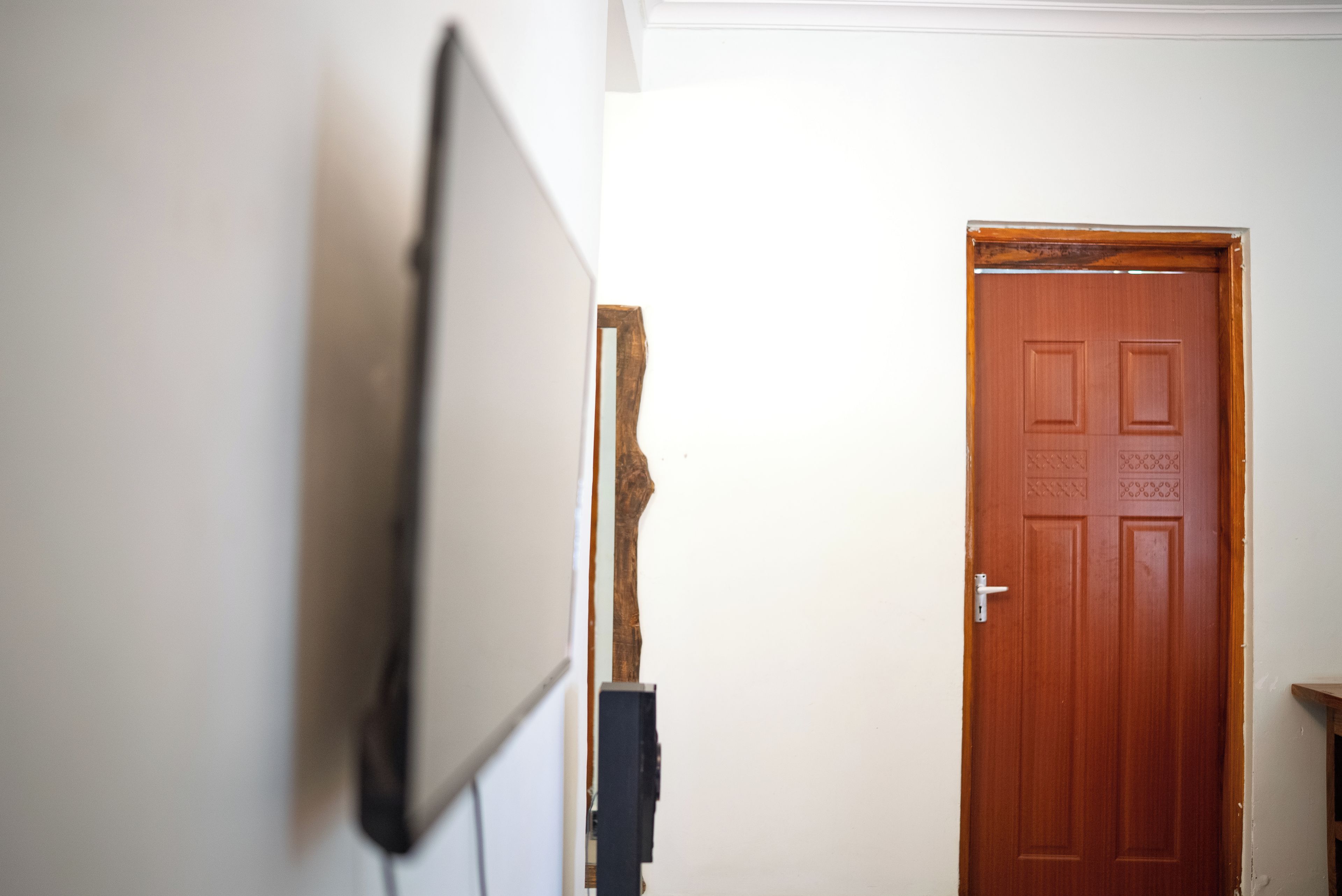Une pièce avec une porte en bois, un mur blanc et un téléviseur fixé au mur.