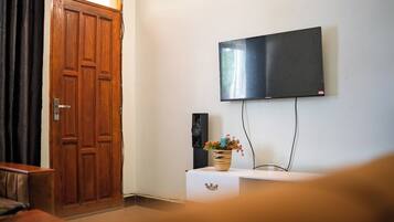 Una habitación con puerta de madera, un televisor de pantalla plana montado en la pared y una pequeña mesa con un jarrón de flores.