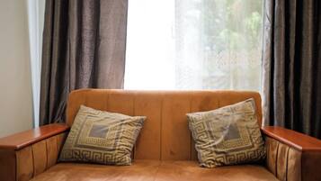 Ein braunes Leder Sofa mit zwei gemusterten Kissen, vor einem Fenster mit durchsichtigen Vorhängen platziert.