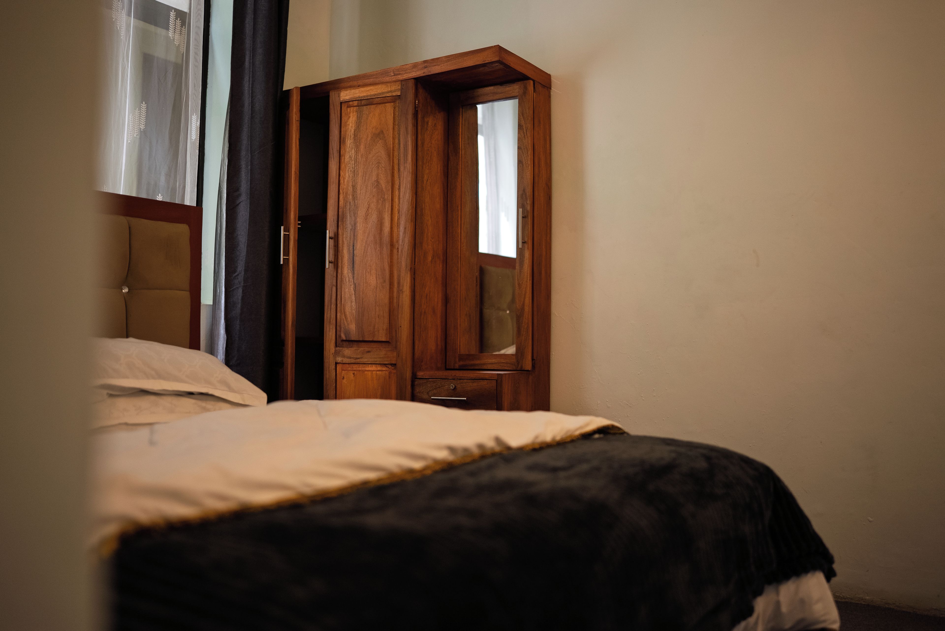 Une chambre à coucher avec un lit, une armoire en bois et une fenêtre avec des rideaux.