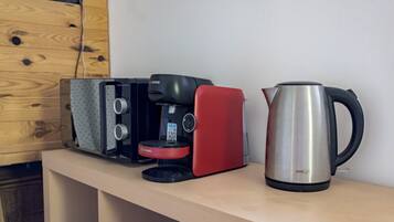 A coffee maker, a red appliance, and a stainless steel kettle on a wooden shelf.