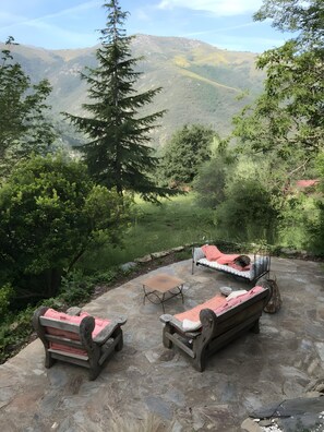 A stone patio with two wooden benches, a metal table, and a metal bed frame with a mattress.