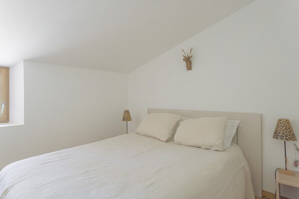 Un dormitorio con cama, dos almohadas, cabecera, decoración de cabeza de venado montada en la pared y dos lámparas sobre mesitas de noche.