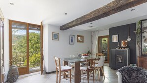 Uma sala de jantar com mesa de vidro, cadeiras de madeira, lareira e vista para o verde lá fora.