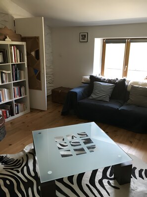 A living room with a sofa, a glass coffee table, a bookshelf, and a window.