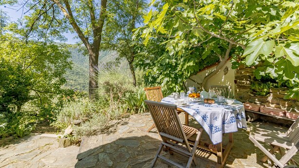 Uma área de refeições ao ar livre com uma mesa posta para dois, cercada por paredes de pedra e vegetação.