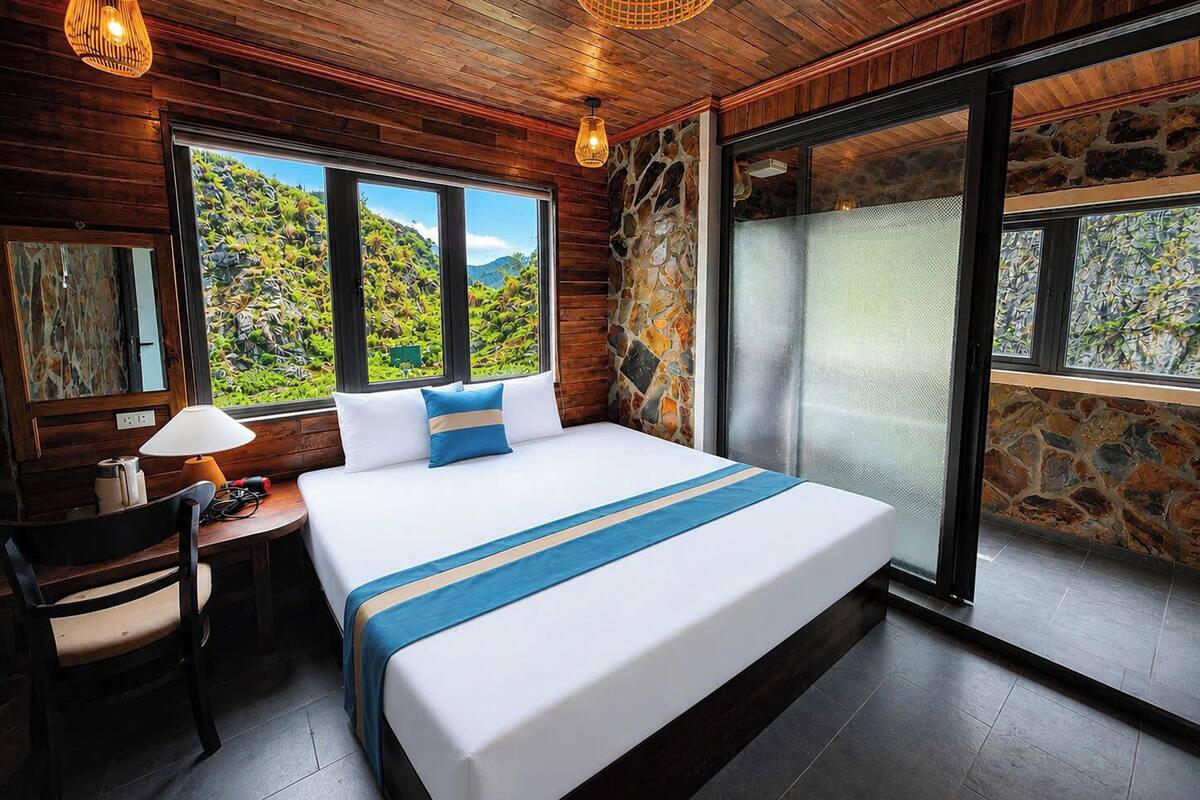 Ein Schlafzimmer mit einem großen Bett, einem Schreibtisch, einem Stuhl, einer Steinwand und Blick auf eine gebirgige Landschaft.