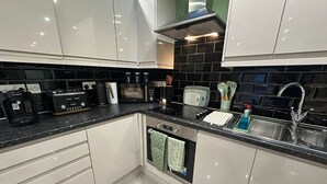 Una cucina moderna con mobili bianchi, zoccolo nero, elettrodomestici in acciaio inossidabile e forno integrato.