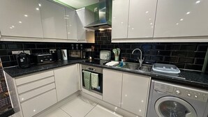 Una cucina moderna con mobili bianchi, un piano di lavoro nero, forno integrato, lavello e lavatrice.