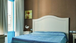 A bedroom with a bed, a nightstand, a wall-mounted lamp, and a window with curtains. - Borgo Rio Favara 6 Luna (Sicilia)