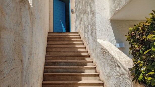 A narrow staircase leading to a blue door, flanked by textured walls and a potted plant. - Borgo Rio Favara 6 Luna (Sicilia)
