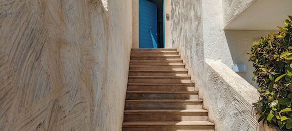 A narrow staircase leading to a blue door, flanked by textured walls and a potted plant. - Borgo Rio Favara 6 Luna (Sicilia)