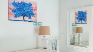 A room with a wall-mounted painting of a tree, a lamp, and a mirror reflecting the painting. - Borgo Rio Favara 6 Luna (Sicilia)