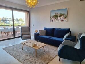 A modern living room with a blue sofa, patterned armchairs, a coffee table, and a cityscape painting on the wall. - 250m² PENTHOUSE DUPLEX- Marbella: 3 bedrooms, 3 bathrooms, solarium, close to the sea, golf courses (marbella)