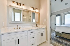 A modern bathroom with a large mirror, two sinks, and a walk-in shower.