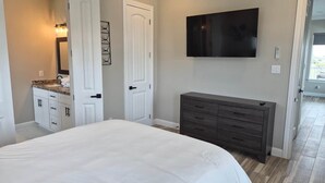 Quarto com cama, penteadeira, televisão e porta.