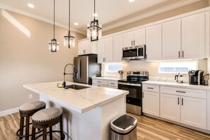 A modern kitchen with white cabinets, stainless steel appliances, a marble countertop, and pendant lighting. - Treasure Island Beach Getaway-Ocean & Island Vibes (Brazoria County)