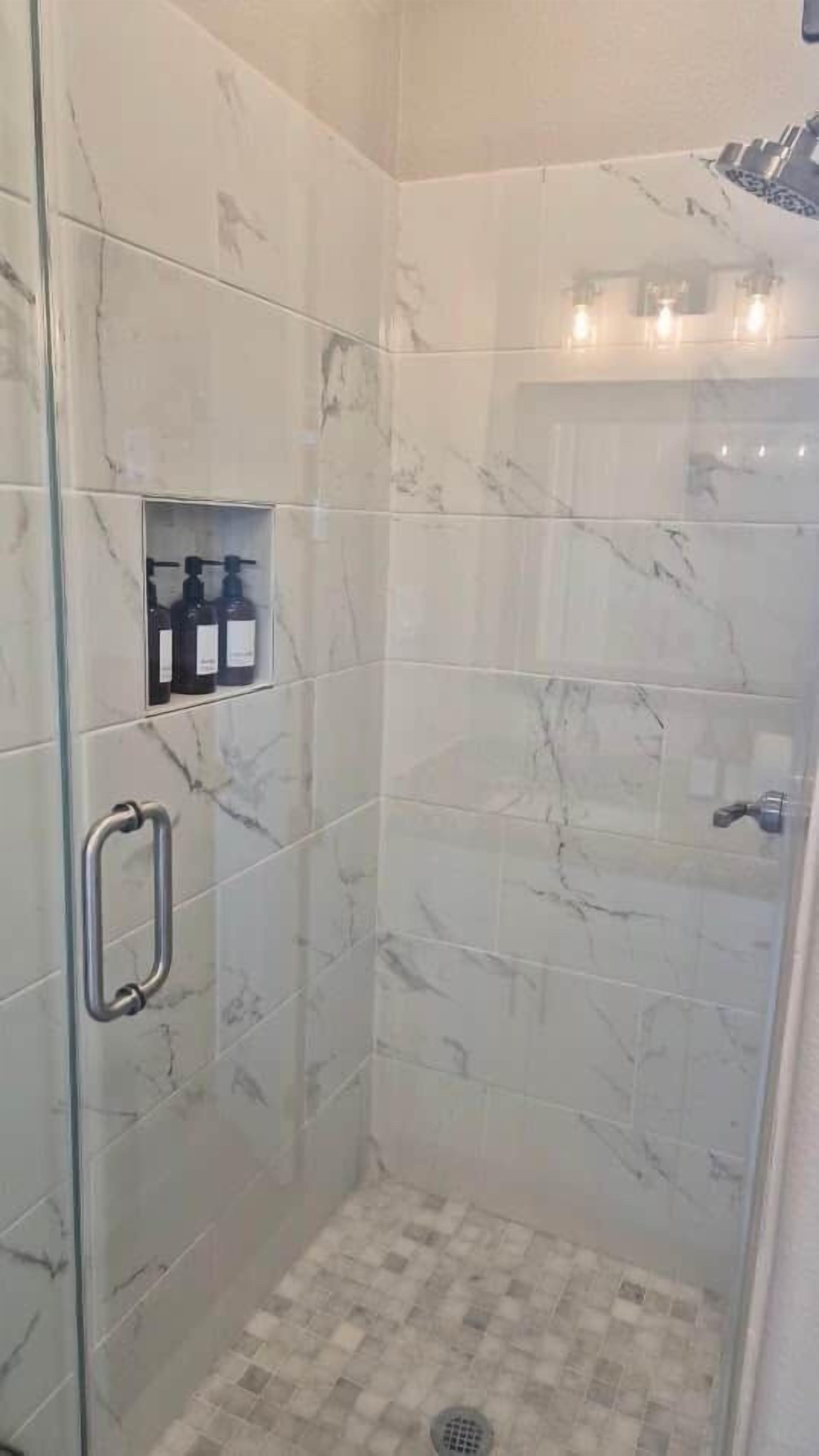 Een inloopdouche met marmeren tegels, een glazen deur, een handgreep en een plankje met toiletartikelen.