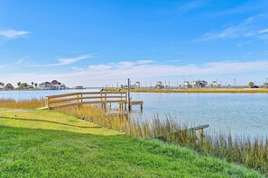 A wooden pier extending into a calm body of water, surrounded by grassy areas and a clear sky.