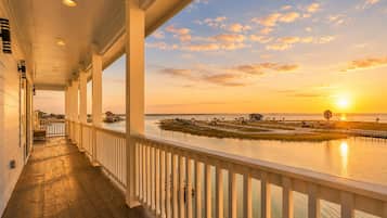 A covered porch with a view of a sunset over water, wooden flooring, and a railing.