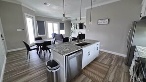 Cozinha moderna com bancada de granito, eletrodomésticos de aço inoxidável e área de jantar com mesa e cadeiras.