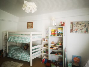 Ein Kinderstockbett mit karierter Bettdecke, ein Bücherregal voller Bücher und Spielzeug sowie eine Wand mit gerahmtem Bild und einem Poster.