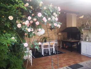 Eine Terrasse mit Tisch und Stühlen, umgeben von üppiger Vegetation und rosafarbenen Rosen.