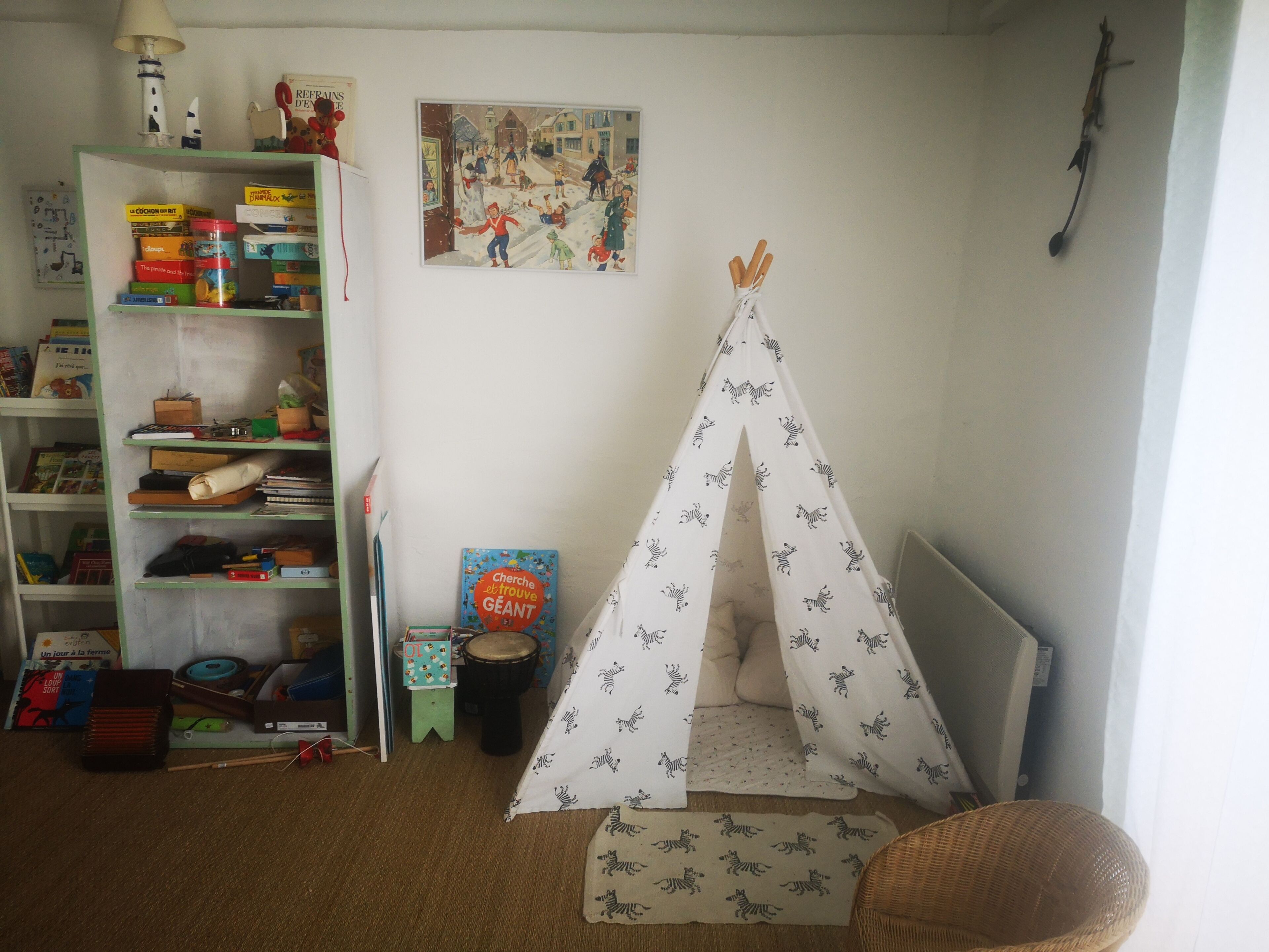Une salle de jeux pour enfants avec une bibliothèque, une tente tipi et un tableau accroché au mur.